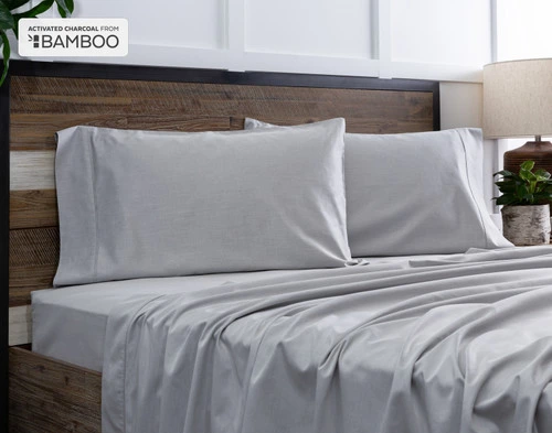 Deux de nos taies d'oreiller Bamboo Cotton avec charbon actif reposent sur un lit en bois avec draps coordonné.