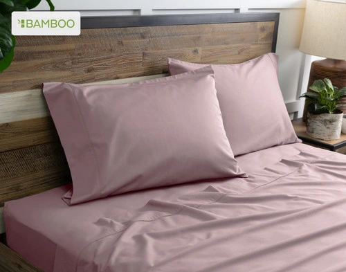 Deux de nos taies d'oreiller Bamboo Cotton en Orchid Purple reposent sur un lit en bois avec draps coordonné.