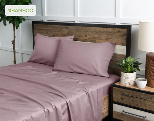 Vue en angle de notre Bamboo Cotton drap  ensemble  en Orchid Purple habillé au-dessus d'un lit en bois dans une chambre à coucher remplie de plantes blanches.