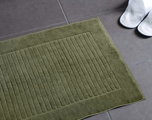 Notre tapis de bain vert en coton modal posé sur un sol de salle de bain gris foncé.