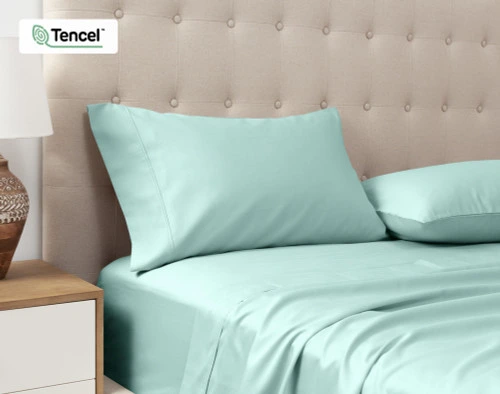 Vue en angle de nos Taies d'oreiller Eucalyptus Luxe TENCEL™ Lyocell en bleu fontaine posées contre la tête de lit d'un lit queen beige.