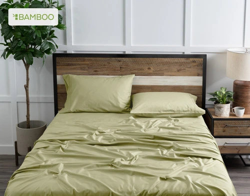 Vue de dessus de notre Bamboo Cotton drap  ensemble  en Elm Green habillé au-dessus d'un lit en bois dans une chambre blanche remplie de plantes.