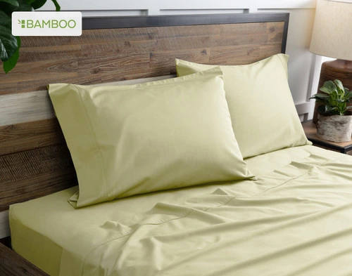 Deux de nos taies d'oreiller Bamboo Cotton en vert orme reposent sur un lit en bois avec draps coordonné.