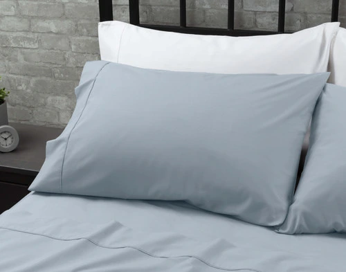 Les taies d'oreiller de notre Coton Percale drap ensemble  en bleu reposant contre deux oreillers blancs en haut d'un grand lit.