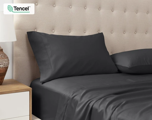 Vue en angle de nos Taies d'oreiller Eucalyptus Luxe TENCEL™ Lyocell en Black Pearl posées contre la tête de lit d'un lit queen beige.