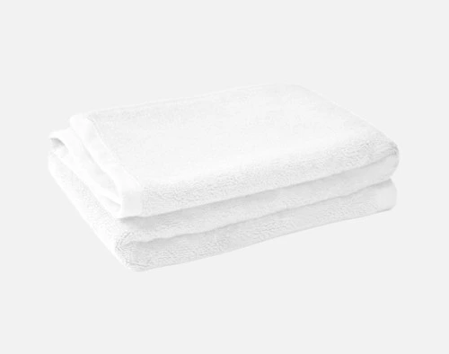 Pile pliée de notre tapis de bain en coton modal blanc sur un fond blanc uni.