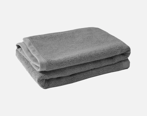 Pile pliée de nos tapis de bain en coton modal de couleur grise sur un fond blanc uni.