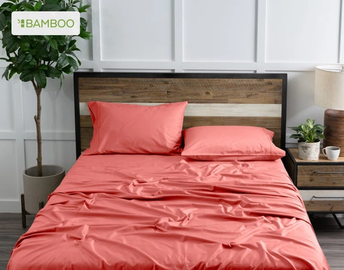 Vue de dessus de notre Bamboo Cotton drap  ensemble  en Hibiscus, un rose rougeâtre léger, habillé au-dessus d'un lit en bois dans une chambre à coucher remplie de plantes blanches.