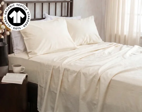 Our Undyed & Unbleached Organic Cotton Sateen Sheet Set dressed over a bed in a natural bedroom near a potted cotton plant.