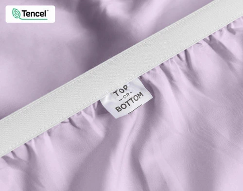 Gros plan sur le bord élastique étiré et l'étiquette indiquant "Top / Bottom" sur notre Eucalyptus Luxe TENCEL™ Lyocell Fitted drap en Lilas.