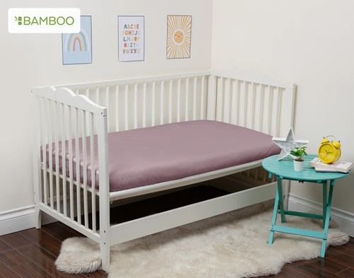 Notre Bamboo Cotton Crib-Sized Fitted drap en Orchid s'habille sur un petit matelas dans un lit d'enfant ouvert.