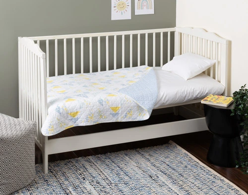 Notre Margot Crib-Sized courtepointe blanc et bleu s'habille sur un petit matelas à l'intérieur d'un berceau dans une chambre aux murs verts et blancs.