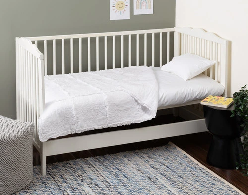 Vue latérale de notre Rosalie Crib-Size Cotton courtepointe drapée sur le matelas d'un petit lit d'enfant.