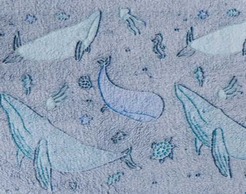 Gros plan sur notre Whale Pod Glow in the Dark polaire Jeté  pour montrer son motif de béluga sur fond indigo.