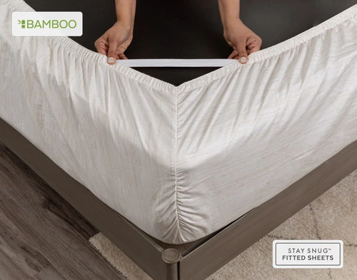 Le coin du matelas retourné est enveloppé de notre Crosshatch Bamboo Cotton drap  ensemble 's fitted drap avec deux mains qui tirent les sangles Snug Fit pour montrer leur élasticité.