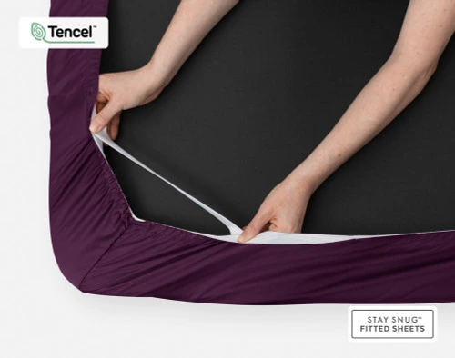 Face inférieure de notre BeechBliss TENCEL™ Modal Fitted drap en Plum avec deux mains montrant la technologie Snug Fit qui le maintient fermement sur le matelas.