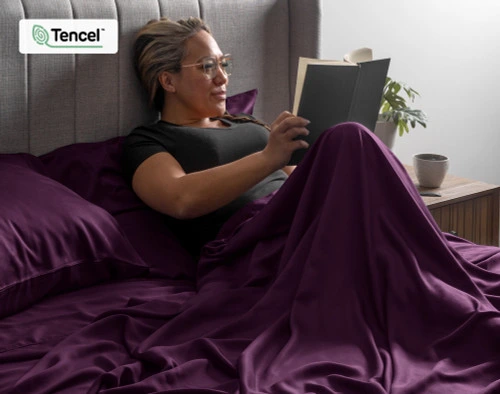 Femme emmitouflée dans notre BeechBliss TENCEL™ Modal drap ensemble  en Plum en train de lire un livre.