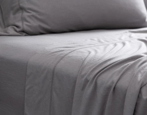 Vue rapprochée de notre Bamboo Cotton Jersey drap ensemble  en gris pour montrer son drap plat drapé sur le côté de son drap ajusté sur un lit queen.