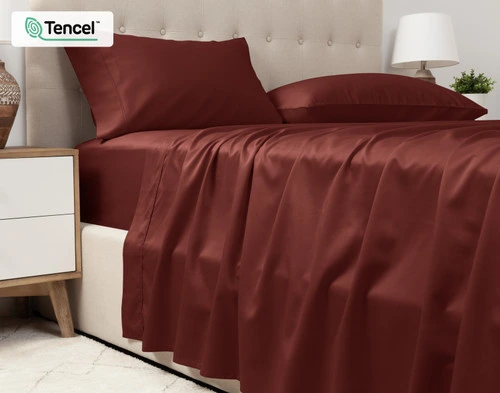 Vue inférieure de notre Eucalyptus Luxe TENCEL™ Lyocell drap ensemble  en Maroon pour montrer son drap plat drapé sur le côté d'un grand lit.