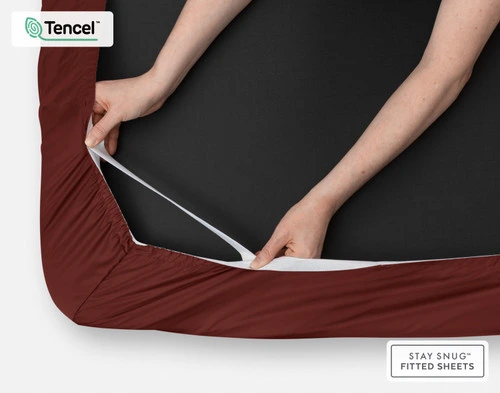 Gros plan sur deux mains étirant l'élastique du coin de notre Eucalyptus Luxe TENCEL™ Lyocell Fitted drap en Maroon.