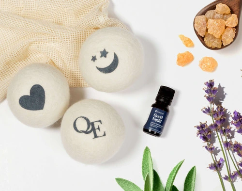 Top view of our Linen Love Wool Dryer Ball Set with fun designs beside its associated laundry blend essential oil made with hints of lavender, sage, and more.