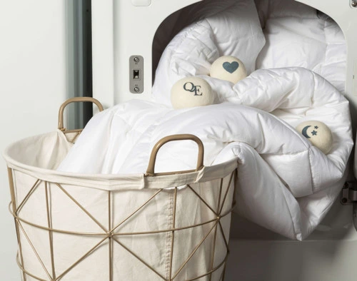 Vue de face de nos boules de laine étalées sur une couette à moitié sortie du sèche-linge et placée dans un panier à linge.