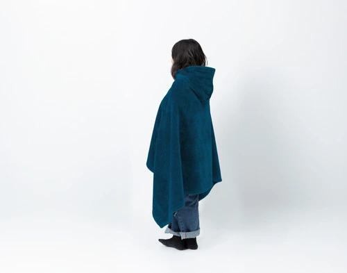 Side view of a young woman wearing our Hooded Cape Plush Wearable Throw in Teal to show its hood.