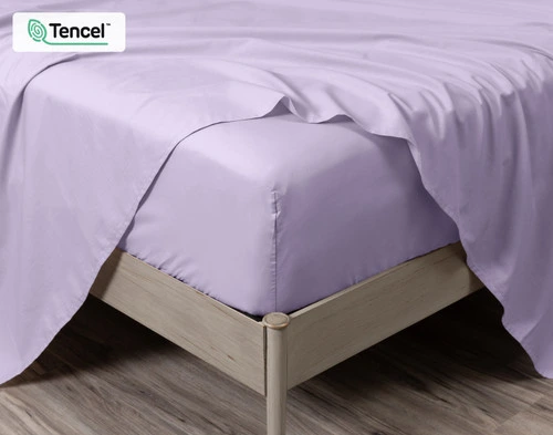 Gros plan sur le coin d'un lit habillé de notre Orchid Cotton Caress drap ensemble  avec un drap plat drapé autour du coin du matelas.