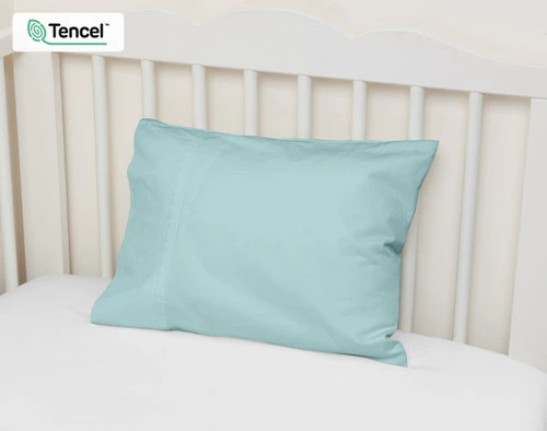 Vue en angle de notre Petite Taie d'Oreiller Eucalyptus Luxe en Shoreline adossée au mur d'un lit d'enfant.