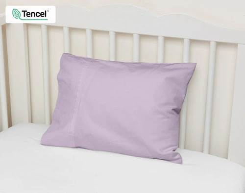 Vue en angle de notre Petite Taie d'Oreiller Eucalyptus Luxe en Lilas adossée au mur d'un lit d'enfant.