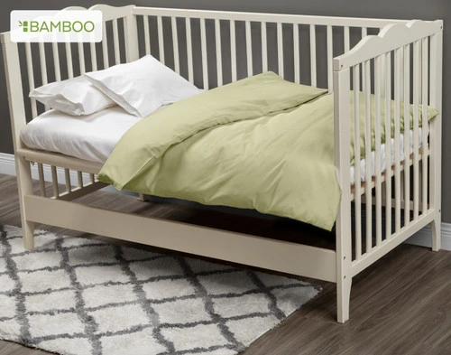 Notre housse de couette pour berceau Bamboo Cotton (Elm Green) habille un petit matelas blanc dans un berceau blanc crème.