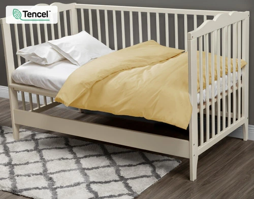 Notre housse de couette BeechBliss pour lit d'enfant Sun Shower habille un petit matelas blanc dans un lit d'enfant blanc crème. 