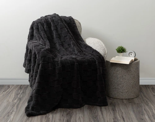 Vue en angle de notre Teddy à carreaux Jeté en anthracite drapé sur un fauteuil gris moderne dans une pièce blanche.