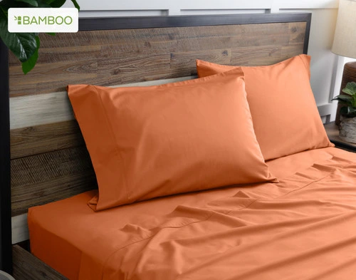 Deux de nos taies d'oreiller Bamboo Cotton en abricot reposent sur un lit en bois avec draps coordonné.