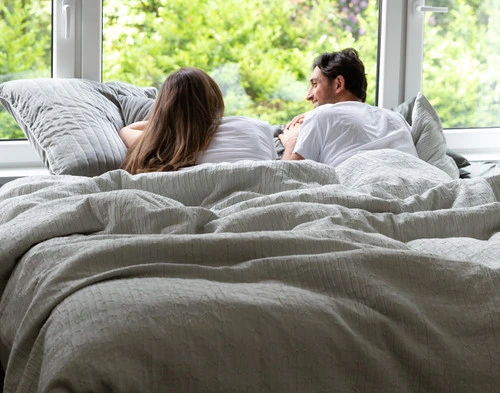 Vue de face de deux personnes dormant sur un lit dans notre housse de couette Montego, assises en avant et faisant face à une fenêtre ensoleillée.