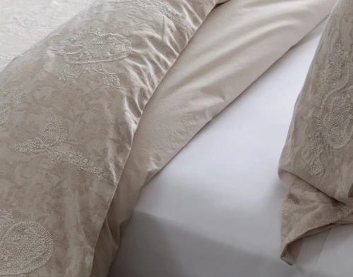 Gros plan sur notre housse de couette Prescott pliée sur un lit à draps blancs pour montrer clairement sa couleur beige ton sur ton.