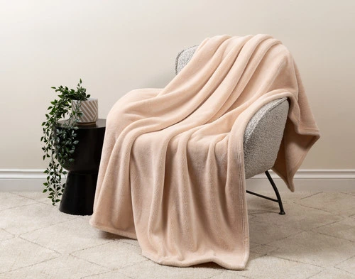 Our Velvet Plush Throw in Rose draped over a beige chair in a white living room.