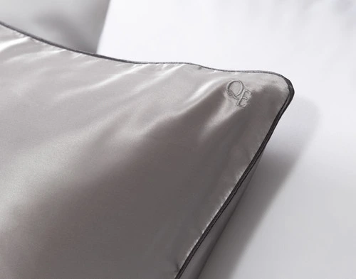 Gros plan sur le logo QE Home brodé sur le coin de notre Silver Soie de mûrier Piped Edge Pillow Sham.