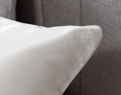 Gros plan sur le logo QE Home brodé sur le coin de notre Snow Soie de mûrier Piped Edge Pillow Sham.