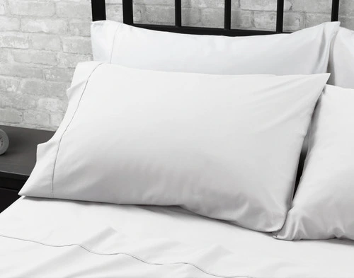 Angled view of a White Organic Cotton Percale Pillowcase fitted over a queen pillow at the head of a matching bed.