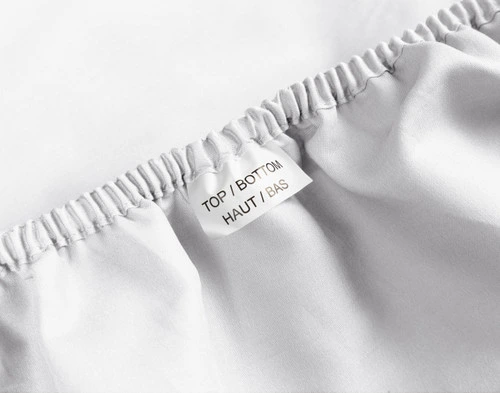 Close-up of a tag reading "Top/Bottom" in English and French along the elastic of our White Organic Cotton Percale Fitted Sheet.