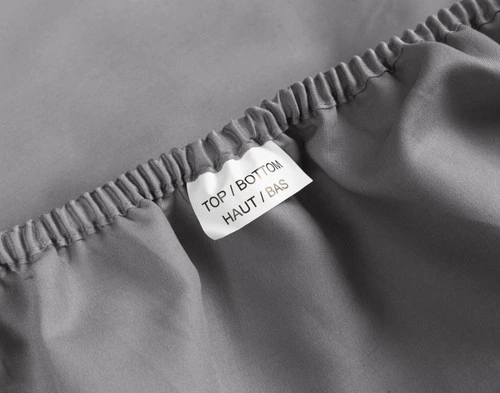 Close-up of a tag reading "Top/Bottom" in English and French along the elastic of our Owl Grey Organic Cotton Percale Fitted Sheet.