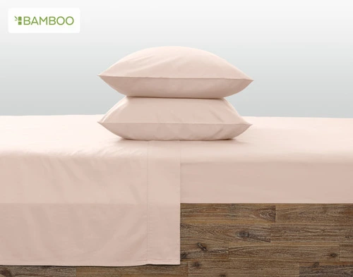 Two pillows in Bamboo Cotton Pillowcases in Rosemist stacked on top of each other on a bed with matching sheets.