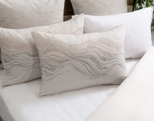 Angled view of our Striation Pillow Sham sitting on a half-dressed white bed.