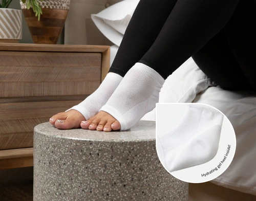 Angled view of a woman's feet wearing our White Hydraheel Spa Socks, with a magnifying glass to show the hydrating inner gel heel.