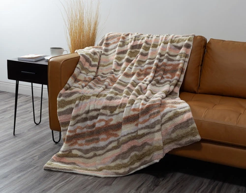 Our Clay Terra Nova Throw draped over  the left side of a couch with its fluffy wave pattern surface facing up.