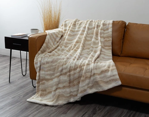 Our Natural Terra Nova Throw draped over  the left side of a couch with its fluffy wave pattern surface facing up.