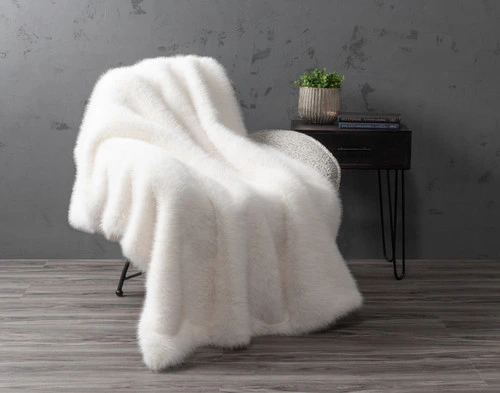 Our ______ Arctic Fox Throw draped over  the left side of a couch with its faux fur surface face-up.