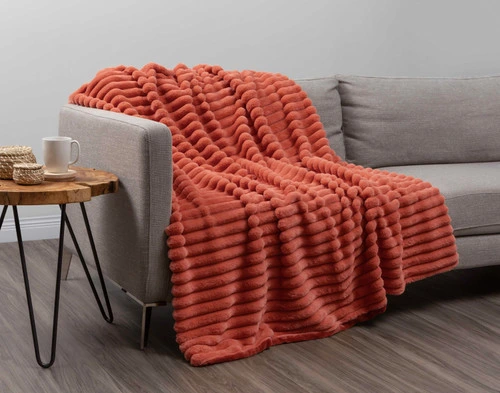 Angled view of our Red Cedar Channel Plush Throw draped over a light grey couch in an empty modern living room.