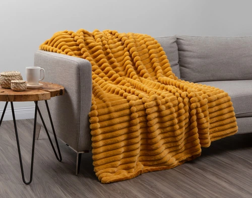 Angled view of our Goldfinch Channel Plush Throw draped over a light grey couch in an empty modern living room.